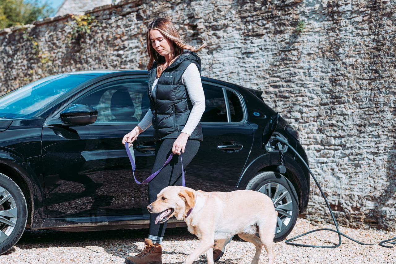 En person går ut och går med hunden, i bakgrunden laddar en svart elbil med Zaptec elbilsladdare