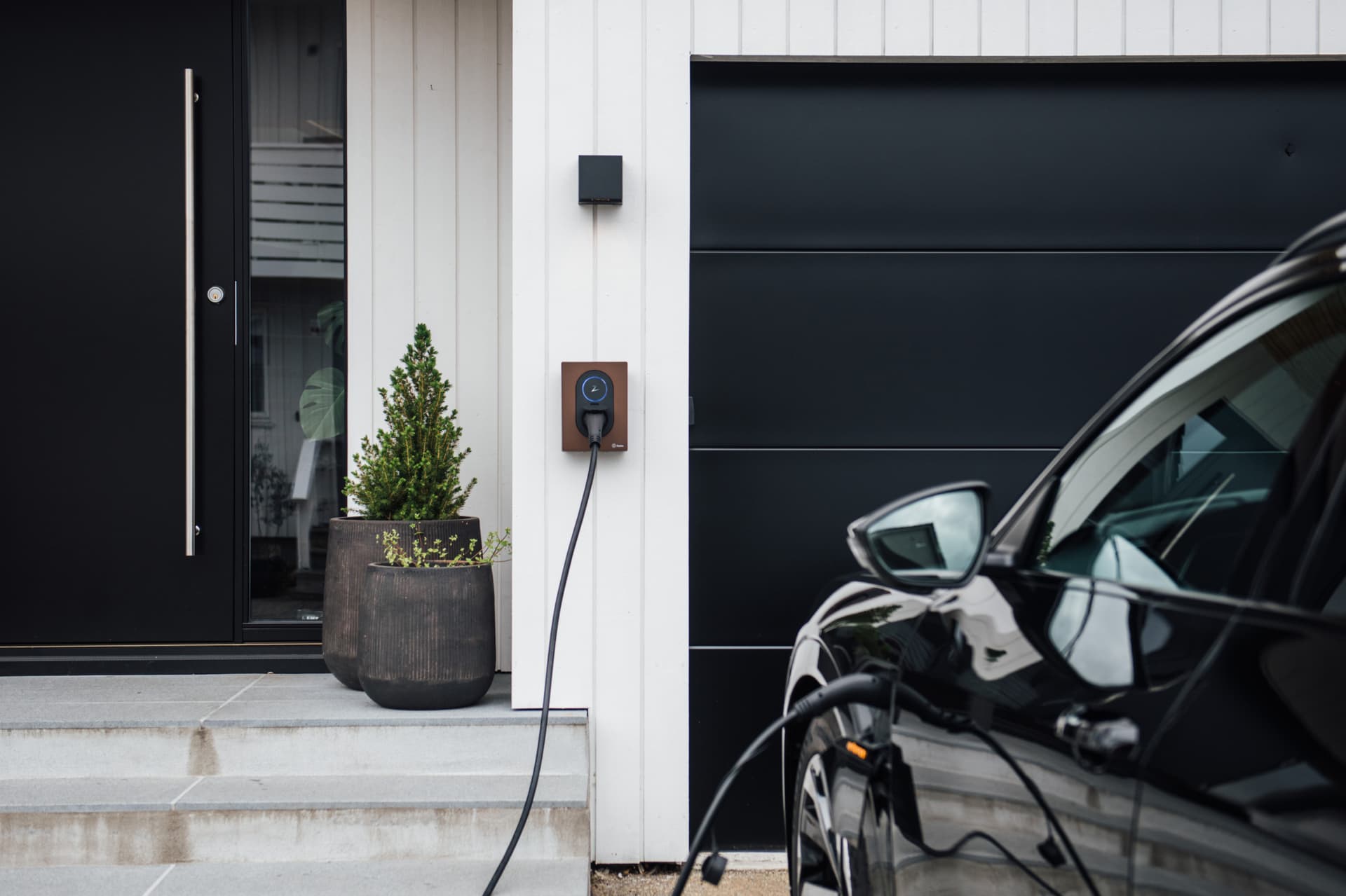 Zaptec Wallbox in braun installiert neben dem Garagentor. Es lädt ein Auto.