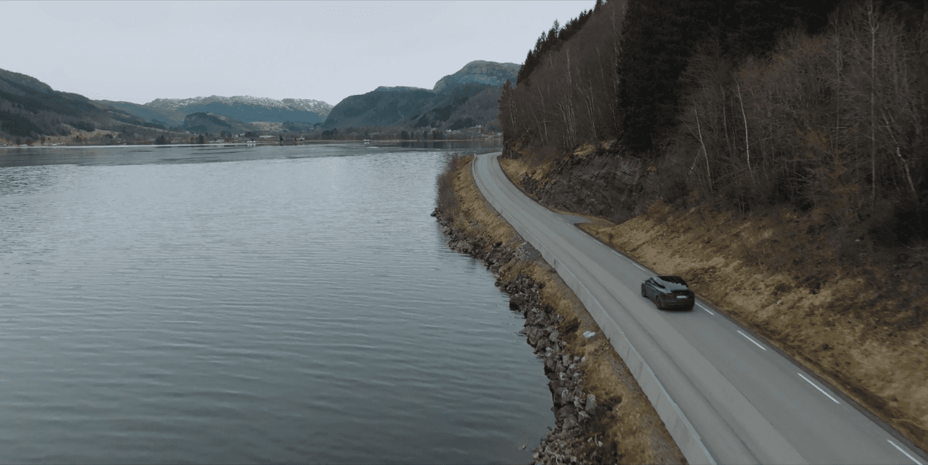 Ein E-Auto-Fahrer fährt unter Reichtweitenangst auf einer Straße an einem See entlang.