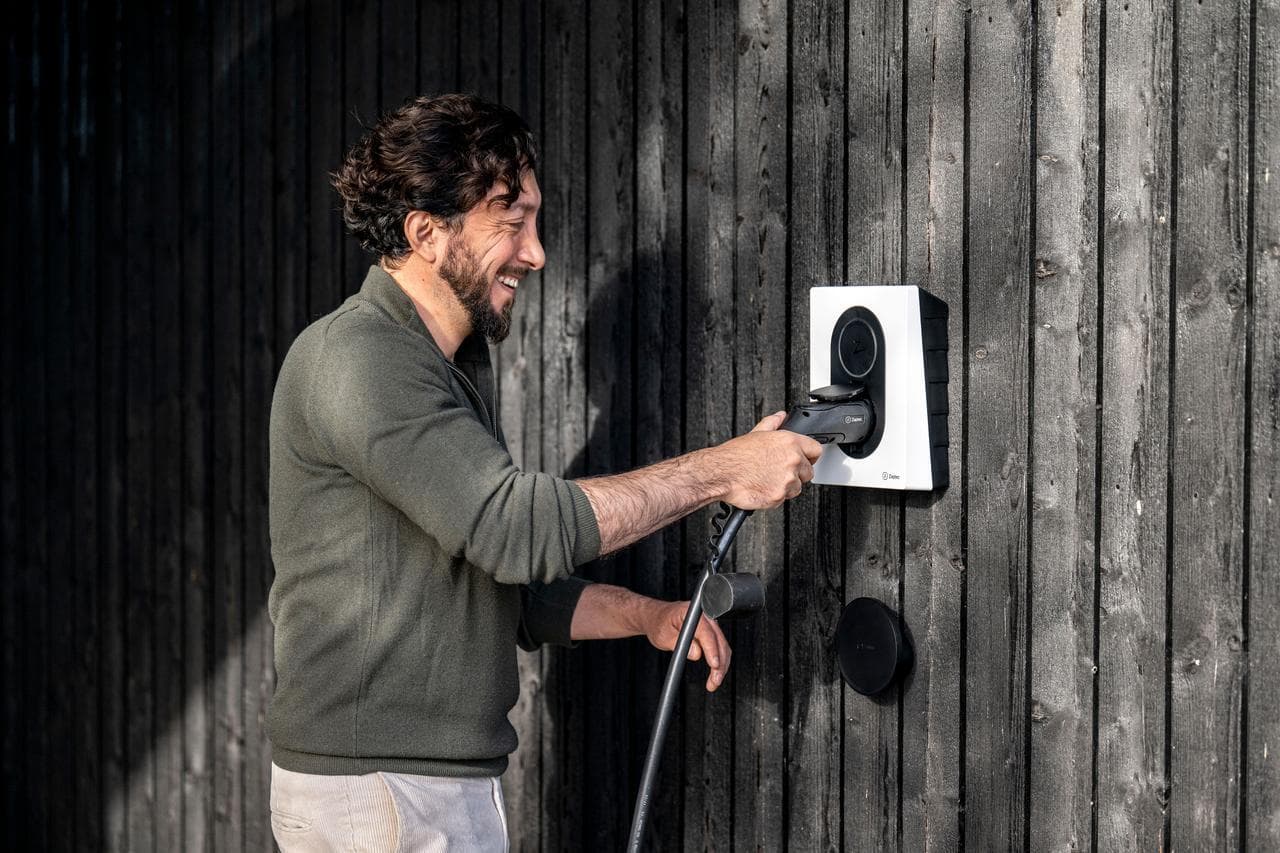 Man laddar en elbil med en Zaptec-laddbox monterad på en mörk trävägg.