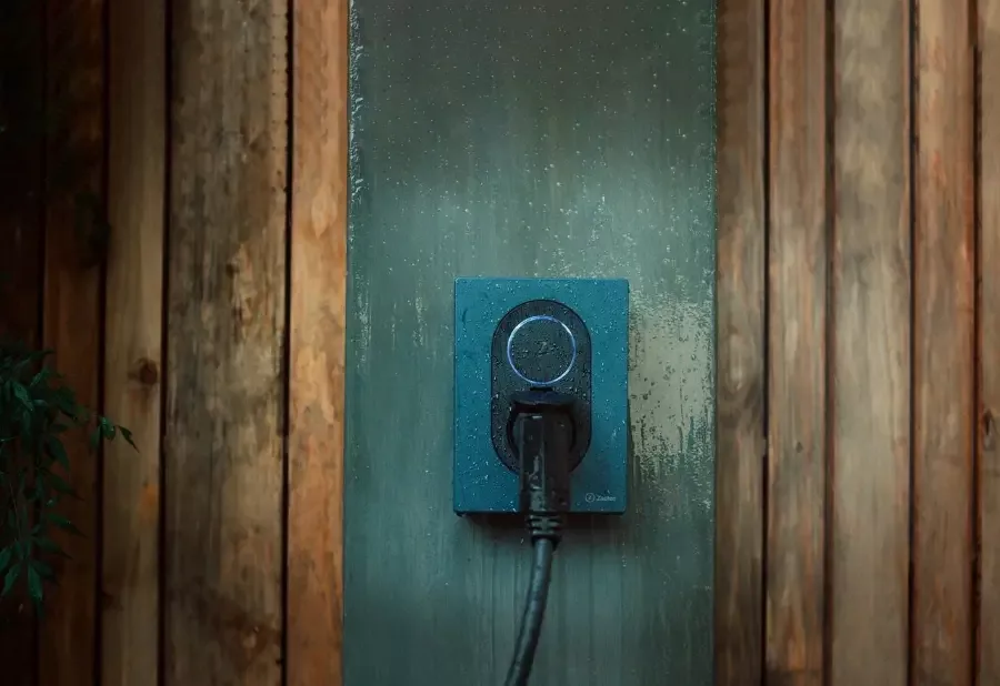 En Zaptec Go laddbox monterad på en vägg, med regndroppar på ytan, där en laddkabel är ansluten till enheten.