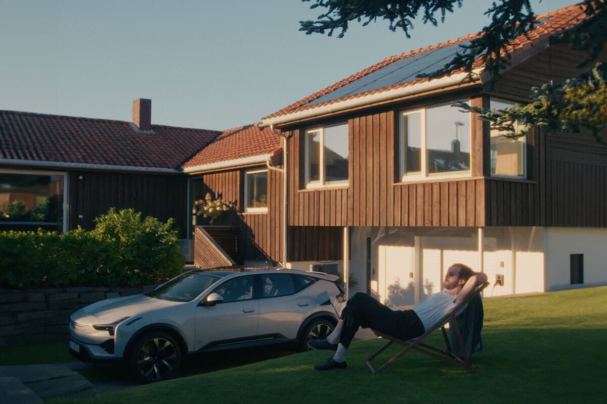Enebolig med solcellepaneler badet i lav kveldssol. Hvit bil står parkert i oppkjørselen. På gressplenen foran huset ligger en person tilbakelent i en solstol.