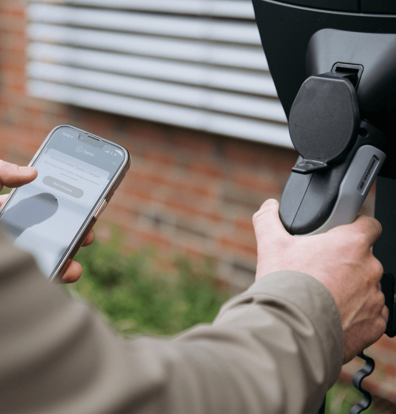 En person holder en ladekabel og en mobiltelefon med Zaptec-appen åpen, klar til å starte lading ved en Zaptec Pro utendørs