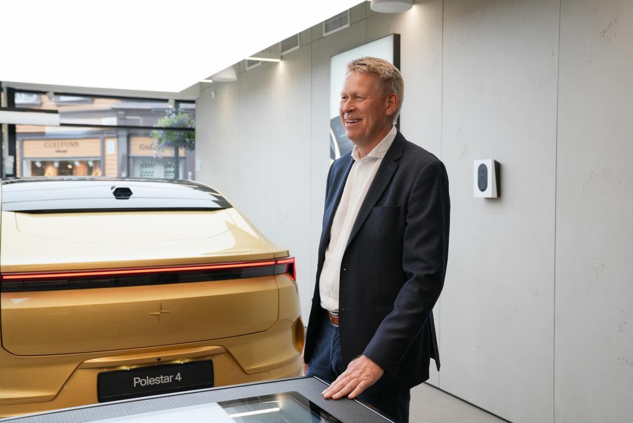 Kurt Østrem CEO Zaptec står med mörk kavaj och vitskjorta i ett Polestar showroom. Brevid honom står en senapsgul Polestar 4 och bakom honom på en ljust grå betongvägg sitter en vit Zaptec Go laddare