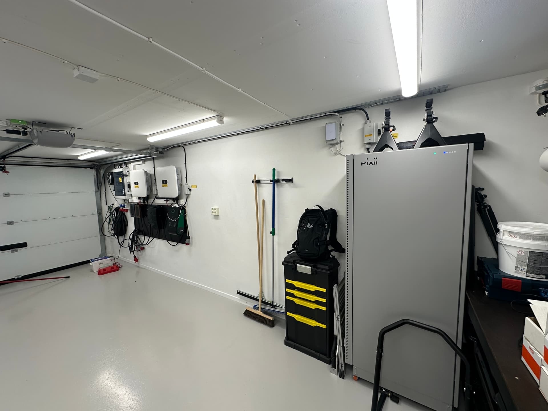 A clean and organized garage with energy system components mounted on the wall, including an inverter and battery storage. The setup indicates a home equipped for solar energy usage and efficient EV charging.