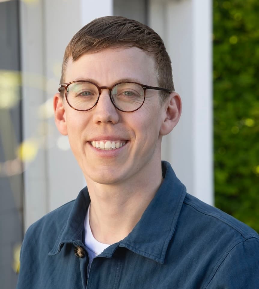 Närbild på Axel Philipson, han står med blå overshirt, glasögon och kollar leende in i kameran