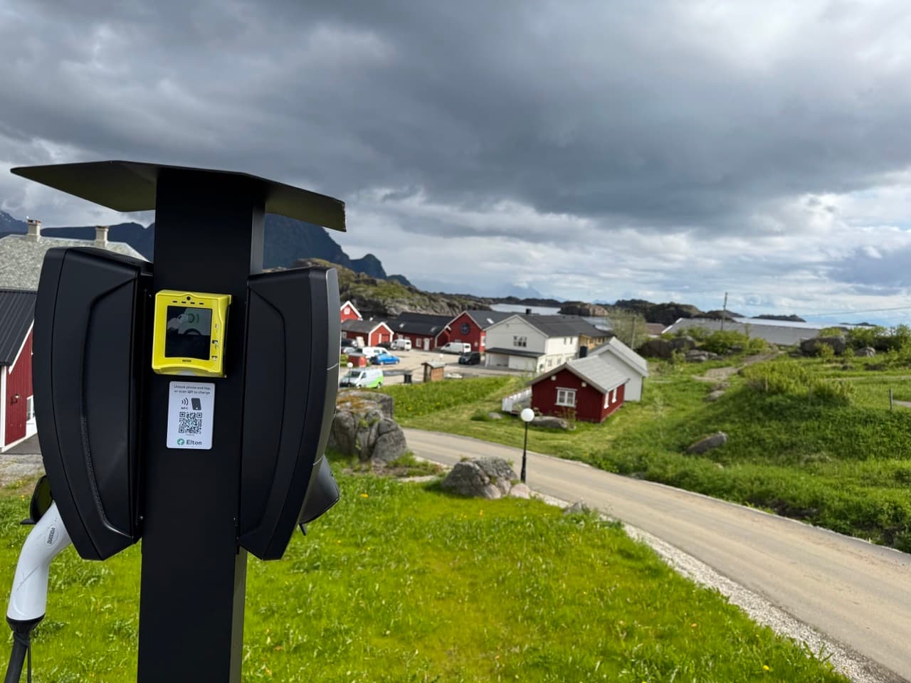 2 stk Zaptec Pro lader montert på stolpe i et grønt landskap med røde og hvite hus, fjell, hav og dramatisk himmel i bakgrunnen
