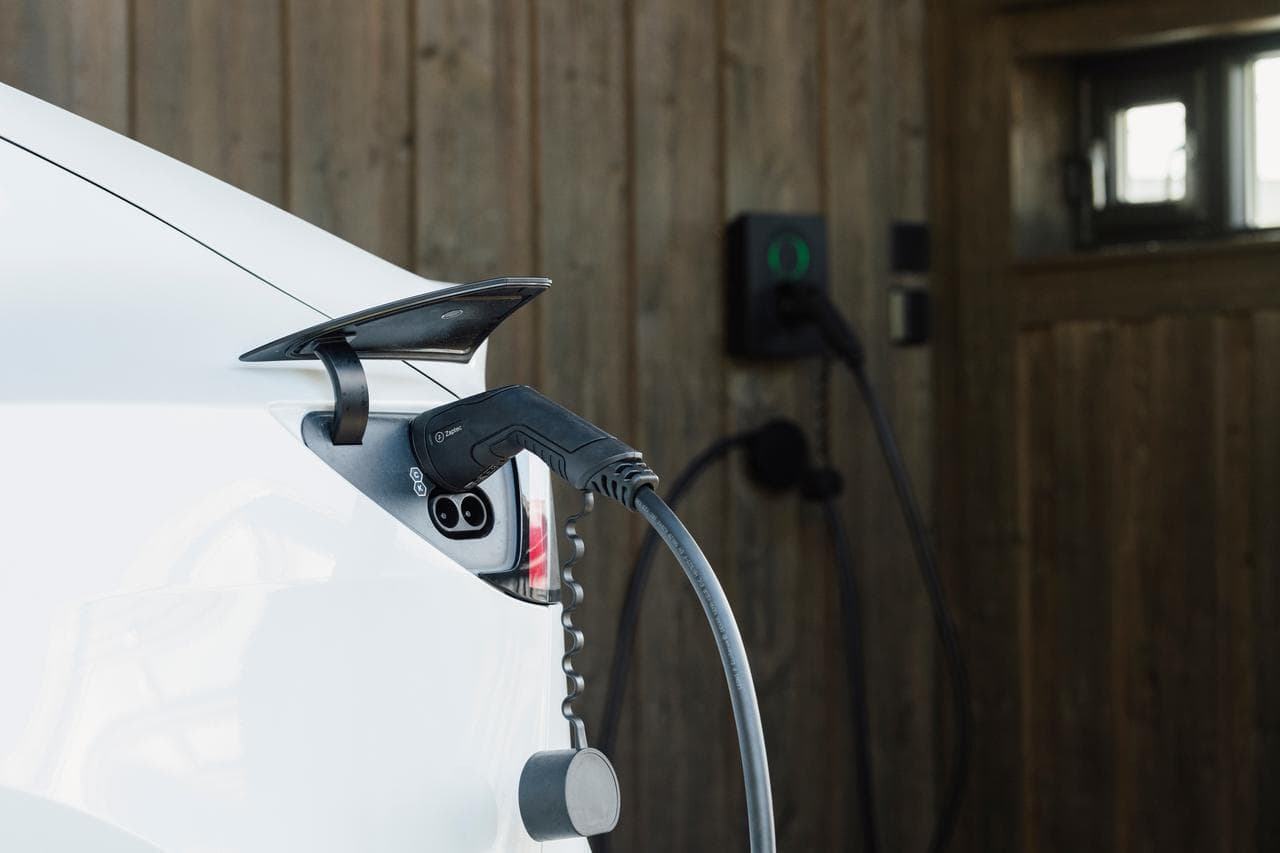 en vit elbil står med laddkabel inkopplad i bilen och i en Zaptec Go laddbox i ett garage med väggar i grått trä.