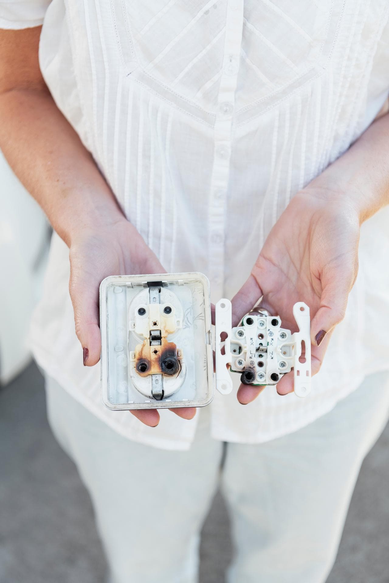 en person i vita kläder håller fram ett bränt eluttag