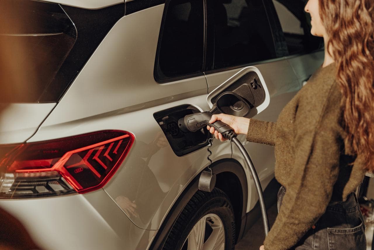 En person i grön tröja kopplar in en Zaptec laddkabel i en vit elbil