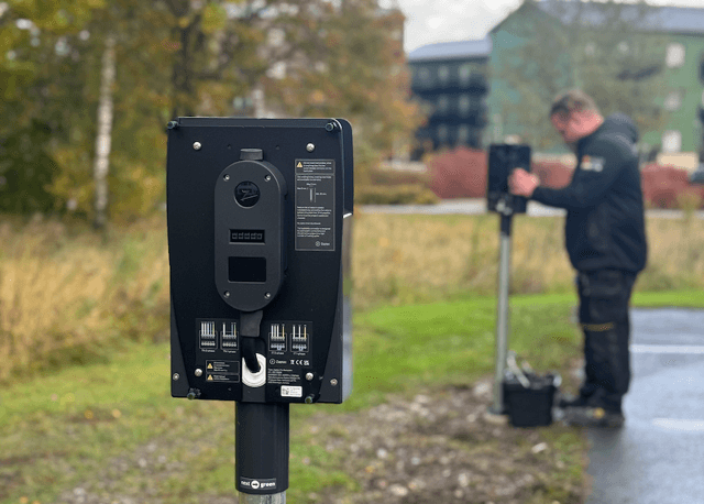 Närbild på en Zaptec Pro bakplatta monterad utomhus, en elektriker arbetar på en annan bakplatta i bakgrunden.