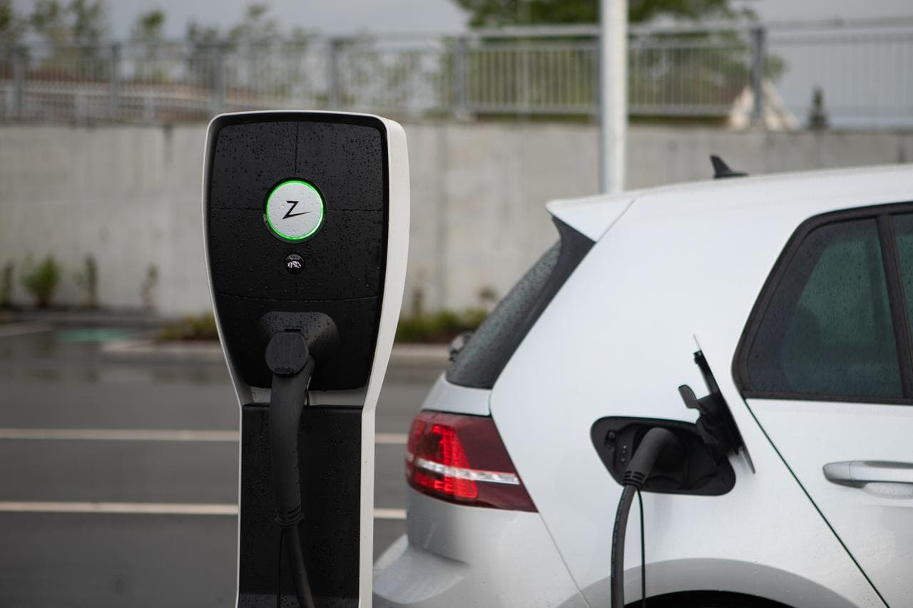 En vit elbil laddas vid en svart Zaptec Pro laddstolpe utomhus i regnet.