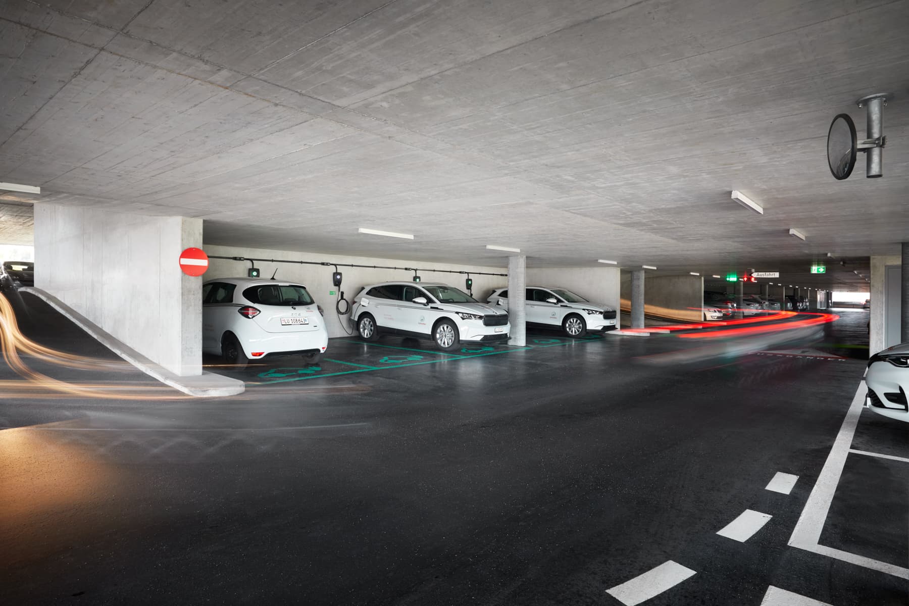 Flere hvite elbiler lades med Zaptec Pro-ladere i et moderne parkeringshus med betongvegger og tydelig veimerking.