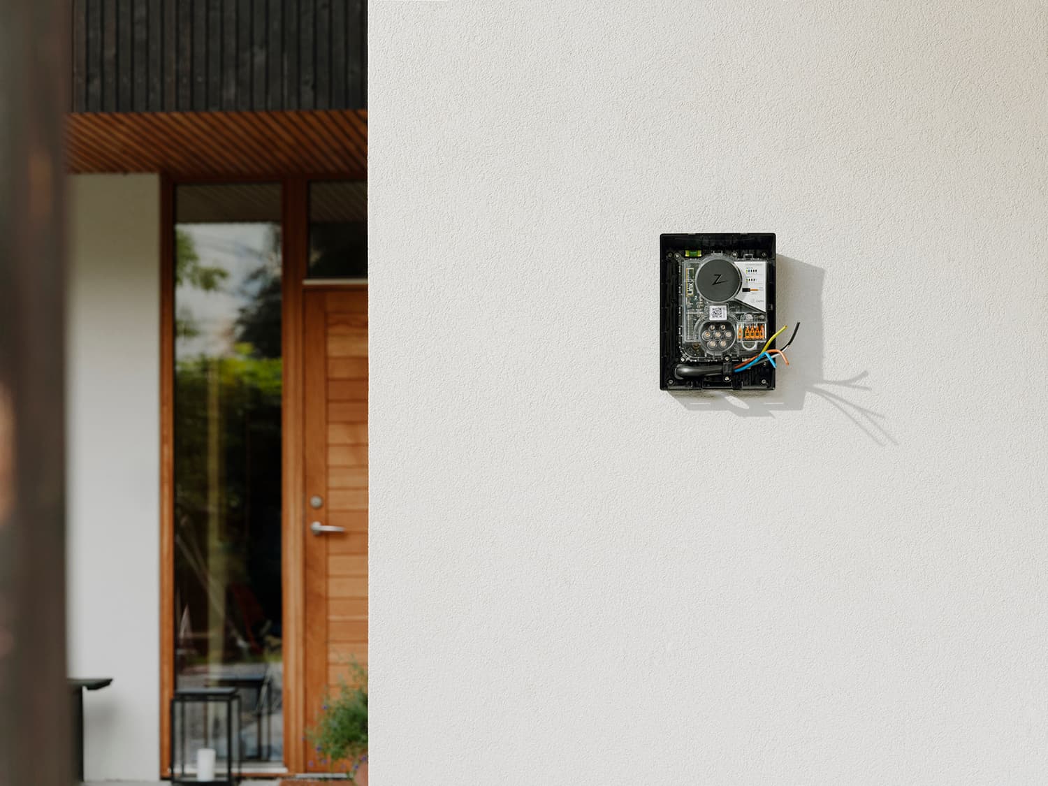 Installation incomplète de borne Zaptec Go sur mur blanc avec fils apparents, porte et fenêtre en bois moderne en arrière-plan.