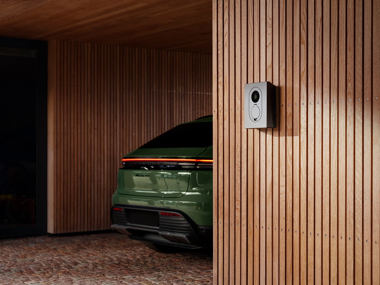 Arrière d’une voiture verte sous carport avec Zaptec Go 2 borne sur mur bois, ombres du soleil sur la scène.