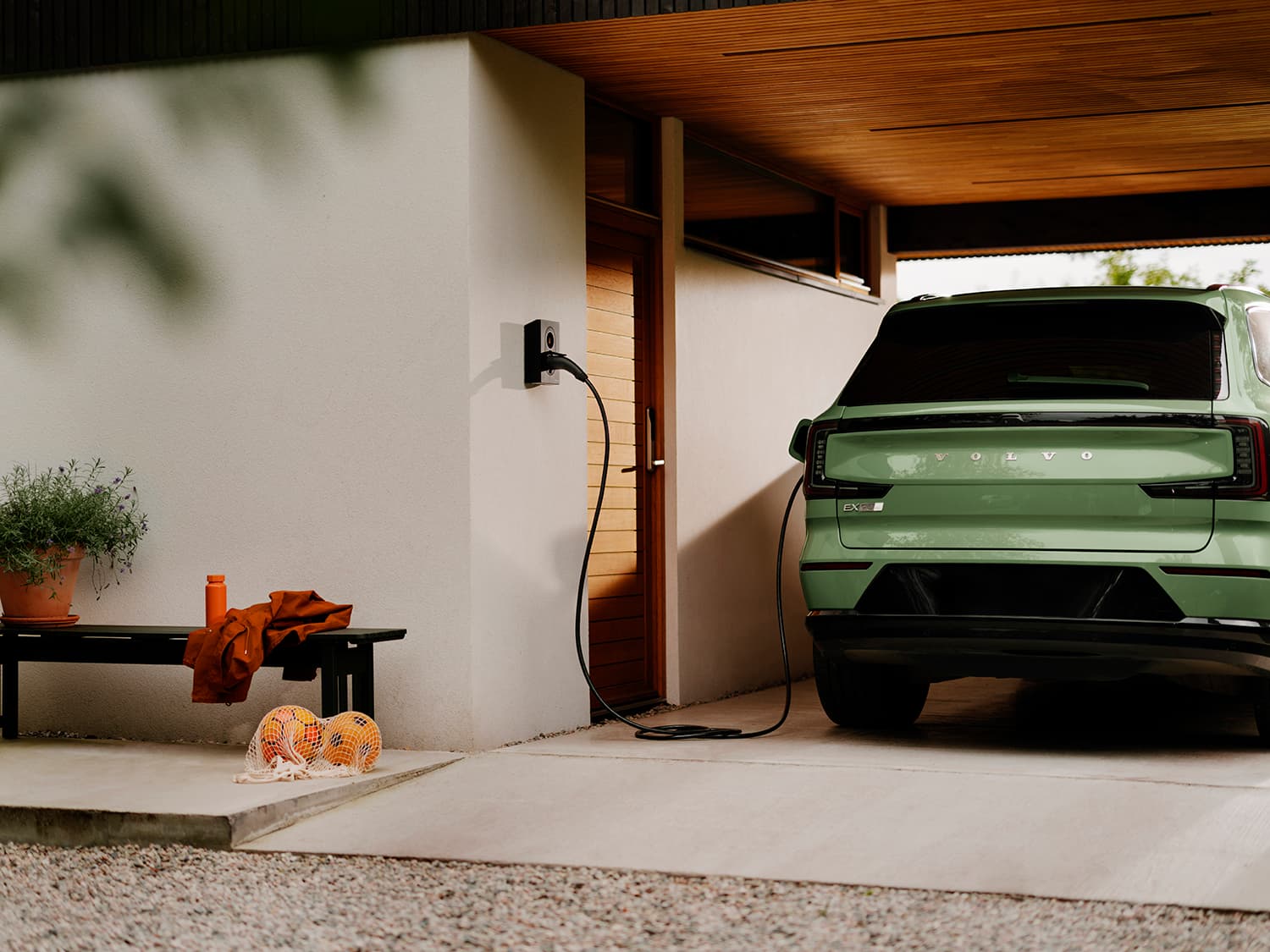 Achterkant van groene Volvo laadt op met Zaptec Go 2 thuislader op witte muur, bank met oranje jas en voetballen ernaast.
