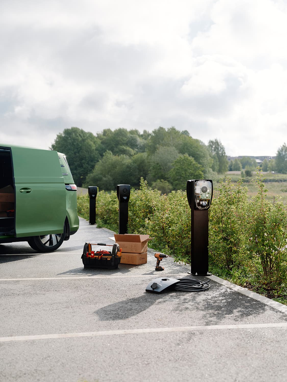 Zaptec Pro Ladestationen auf Säulen im Parkplatz, grüner Transporter, Werkzeuge und Kartons im Vordergrund, Installation läuft.