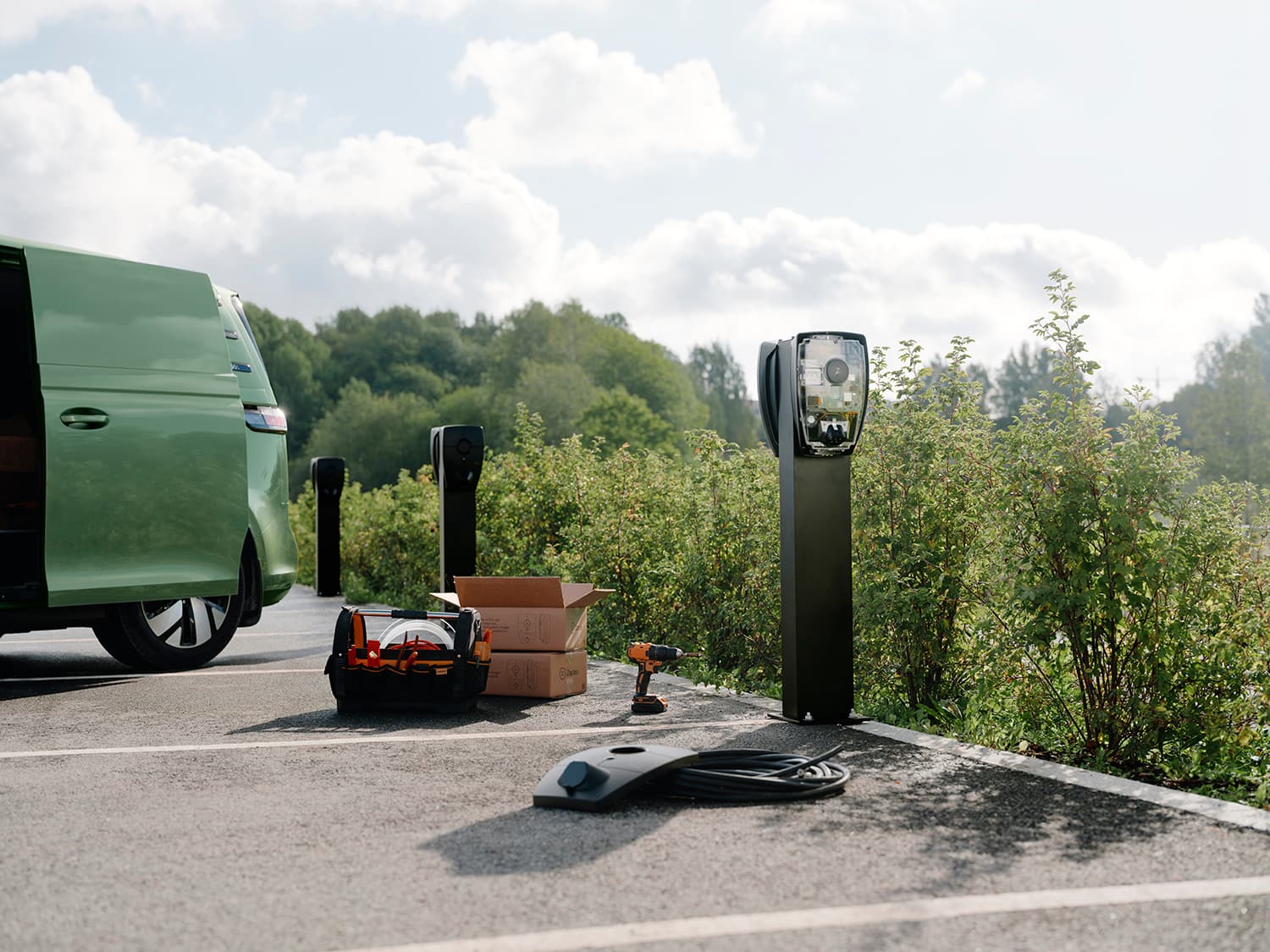 Zaptec Pro charger mounted on column in parking lot, green van, tool box, cardboard box, and charger cover on ground, installation scene.