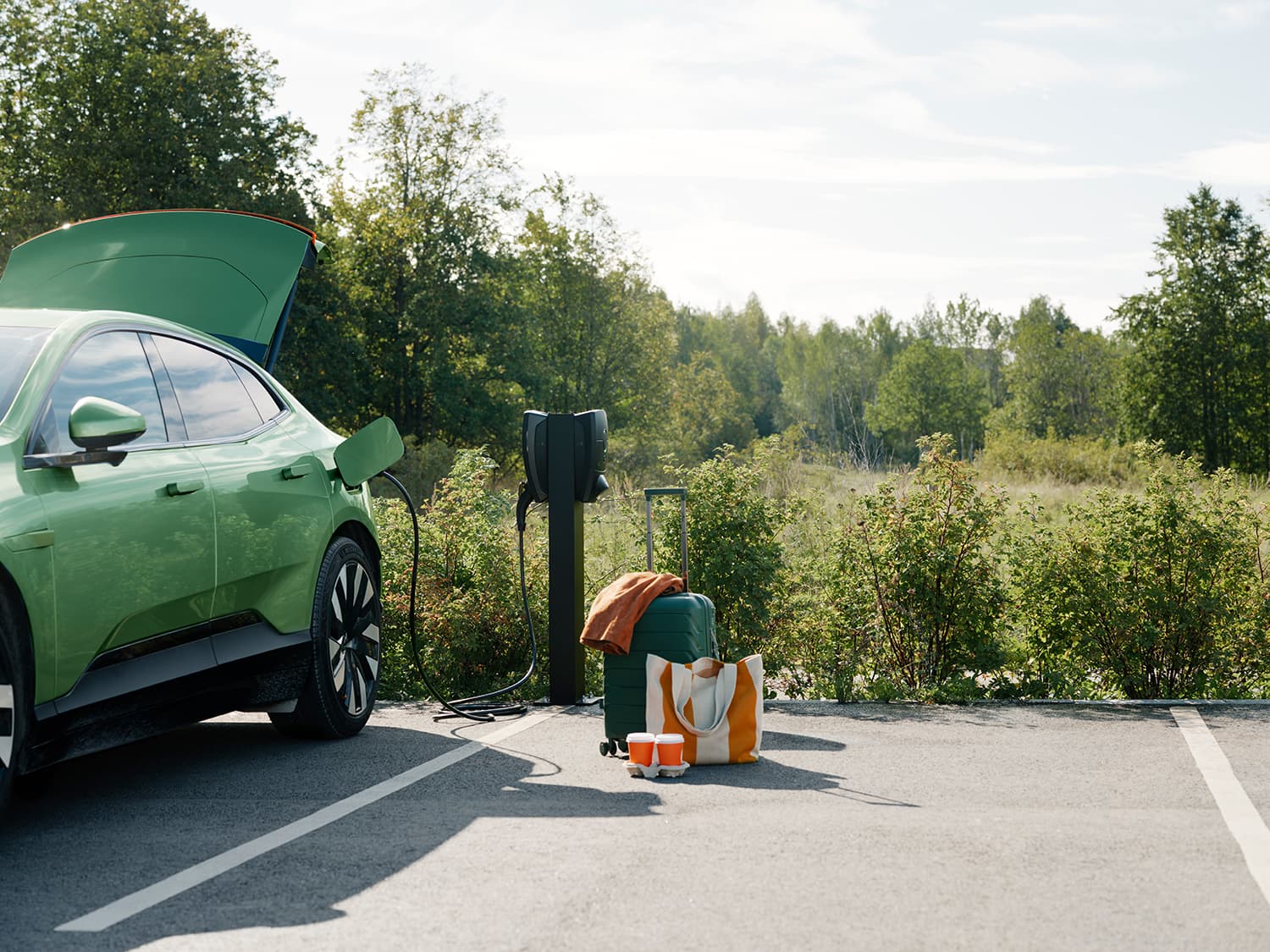 Grünes Auto lädt an Zaptec Pro Ladestation auf Säule im Parkplatz, Koffer, Tasche und Becher am Boden, Kofferraum offen.