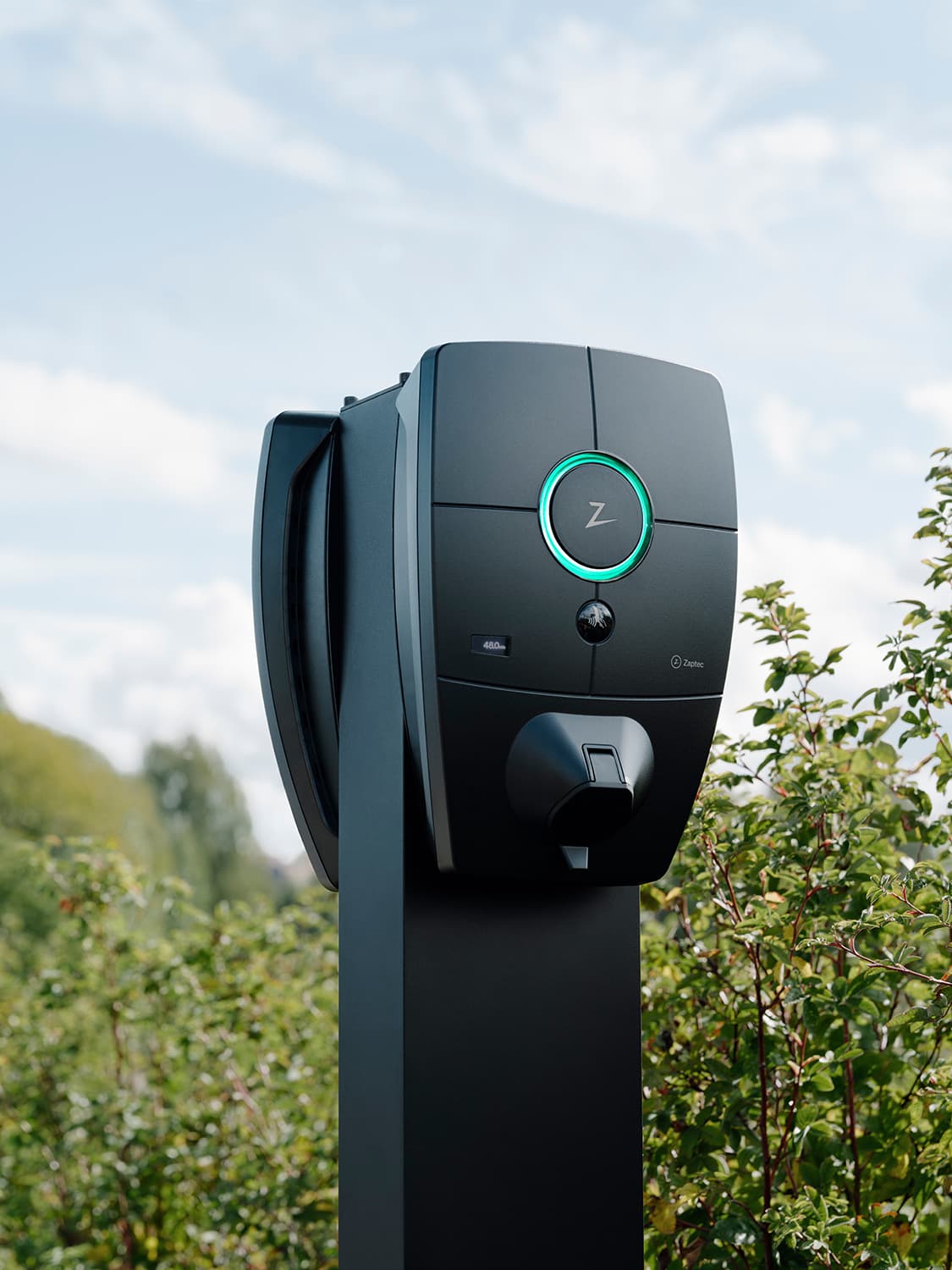 Close-up van Zaptec Pro lader op kolom op parkeerplaats, groene lichtring, groen en blauwe lucht op de achtergrond.