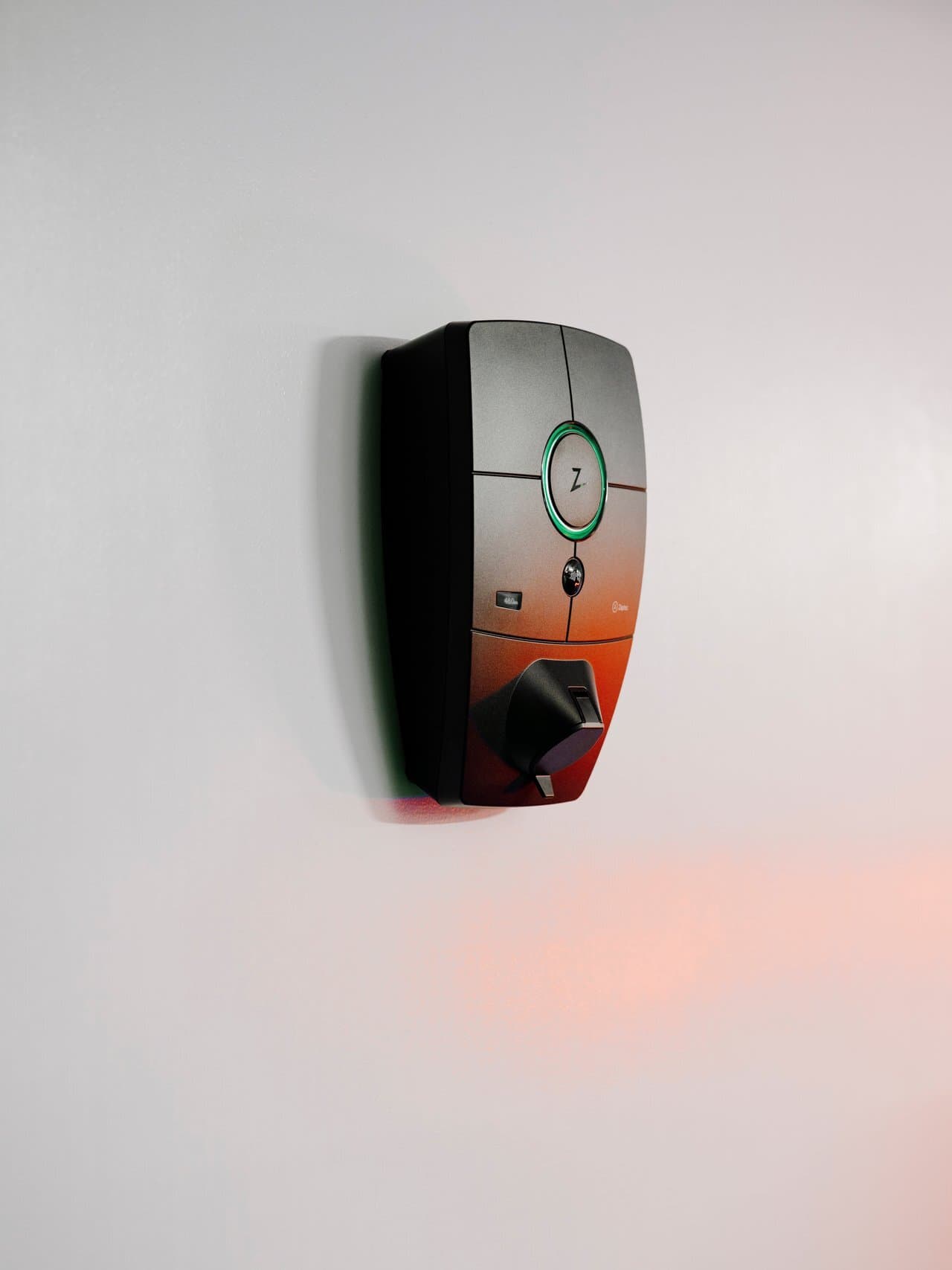 Borne Zaptec Pro sur mur blanc, éclairée par une lumière rouge, ambiance minimaliste de parking intérieur.