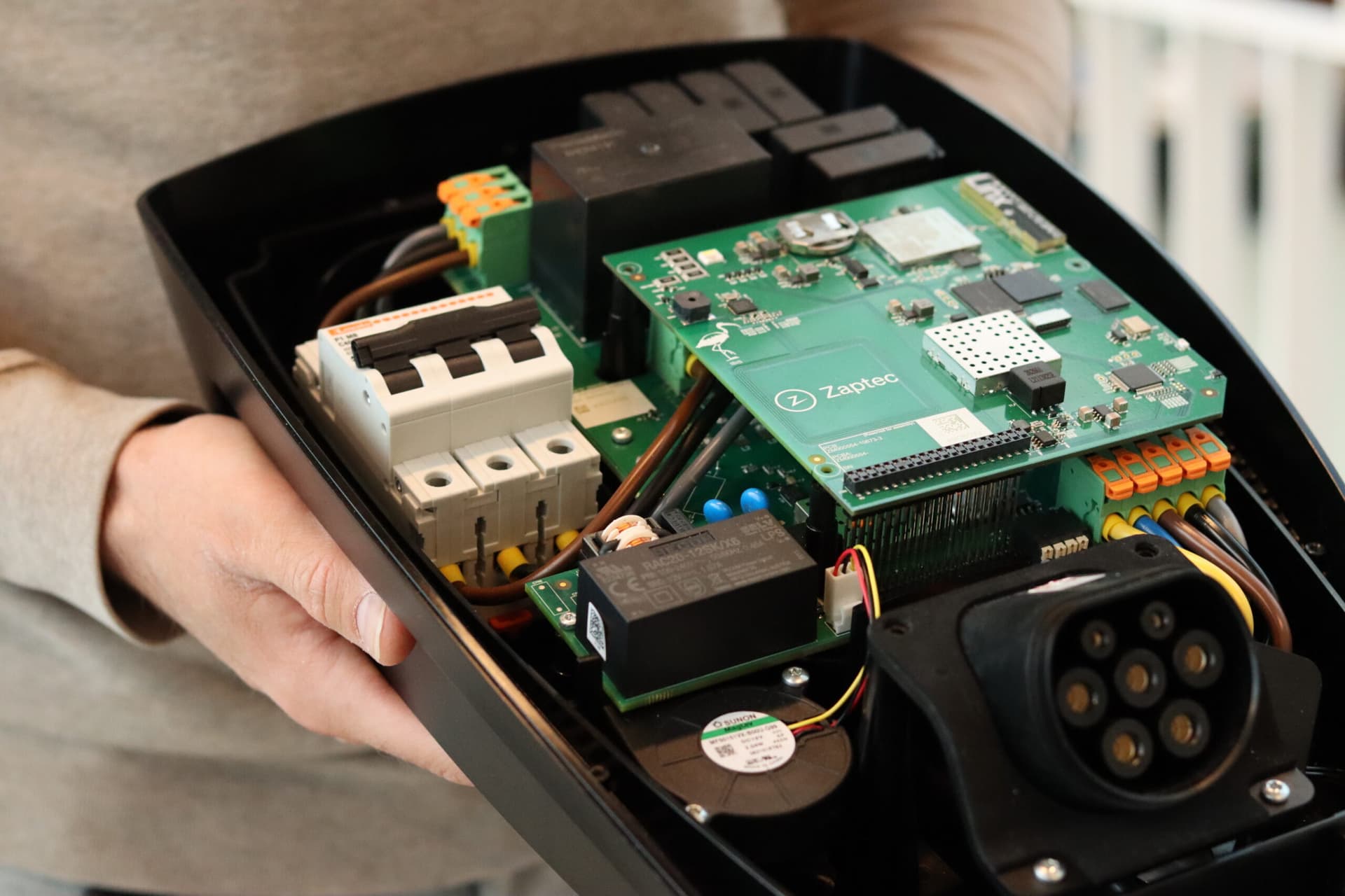 En person i beige tröja håller fram en Zaptec Pro laddare utan lock