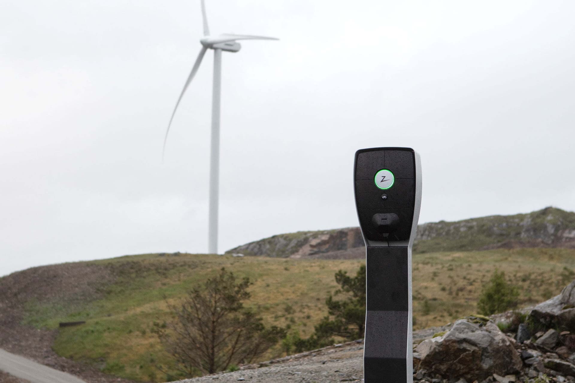 en Zaptec pro laddstolpe sitter monterat i en karat landskap, i bakgrunden syns ett vindkraftverk.