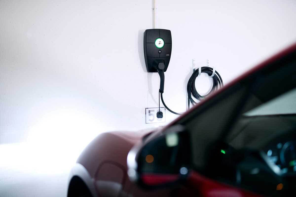 på en vit vägg sitter en Zaptec Pro laddare monterad inkopplad i den via en svart laddkabel från Zaptec står en röd elbil.