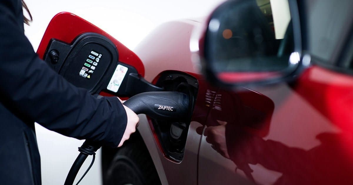 en person håller en Zaptec laddkabel som sitter i en röd elbil