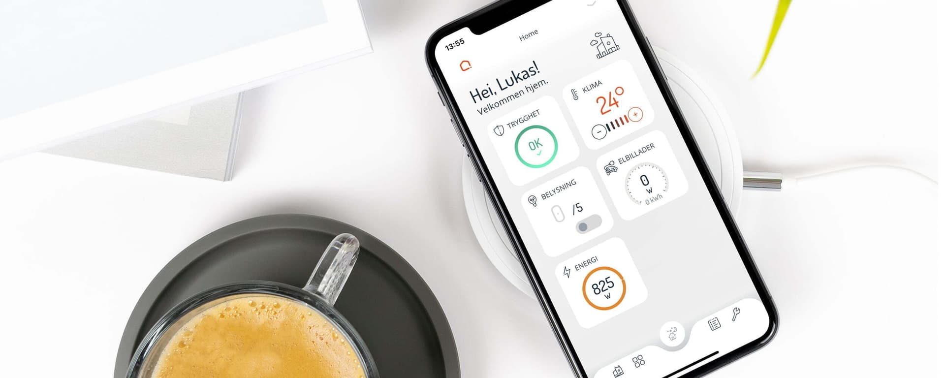 En smarttelefon ligger på en trådløs lader med Zaptec-appen åpen, som viser ladestatus og energiforbruk. Ved siden av står en kopp kaffe på et hvitt bord i et lyst miljø.