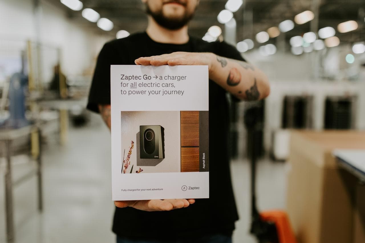 En person med skägg står i en fabriksmiljö och håller fram en Zaptec Go förpackning som är i huvudfokus på bilden.