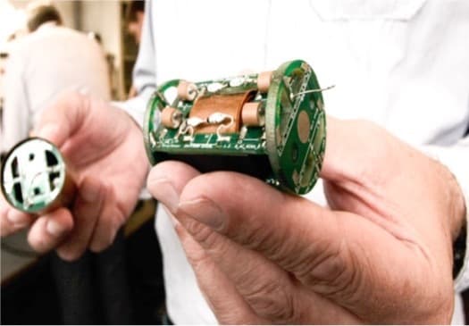 En person holder en elektronisk komponent med synlige kretser og kobberspoler