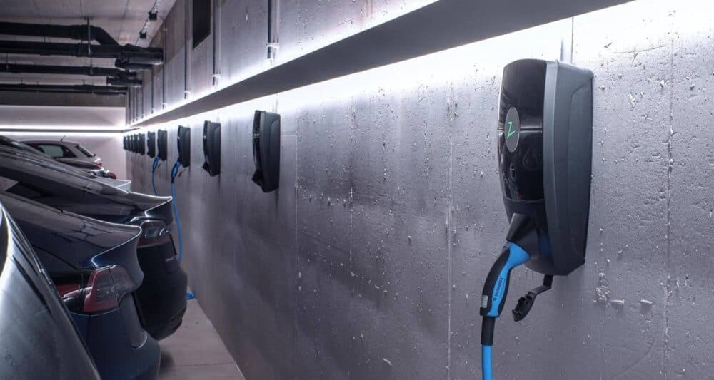 ett parkeringsgarage med en belysningslist som går längsmed väggen under belysningen sitter två Zaptec pro laddare, i den ena laddaren är en svart elbil inkopplad.