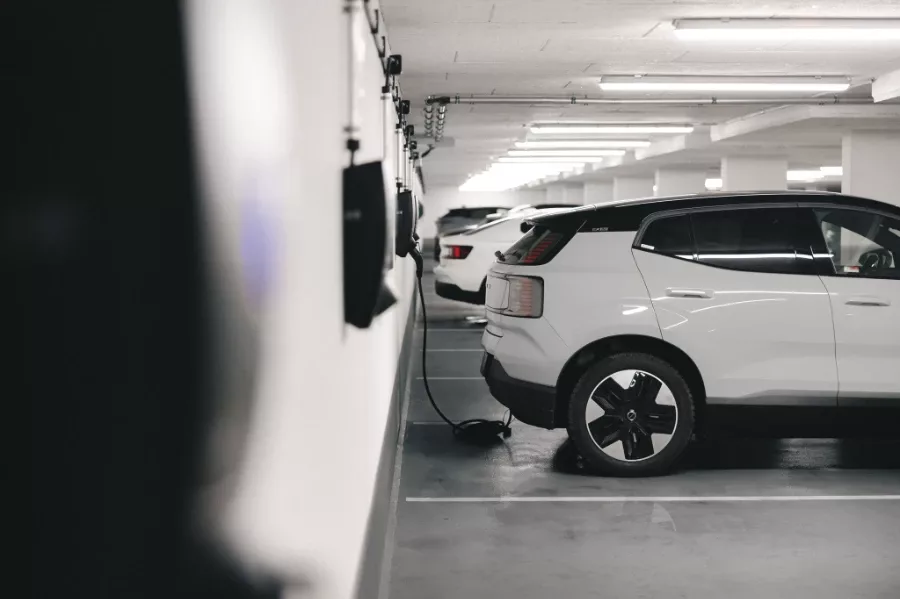 En Volvo EX30 parkerad i ett garage och laddas via en Zaptec Pro laddbox. Bilen är vit med svarta detaljer på hjulen och karossen.